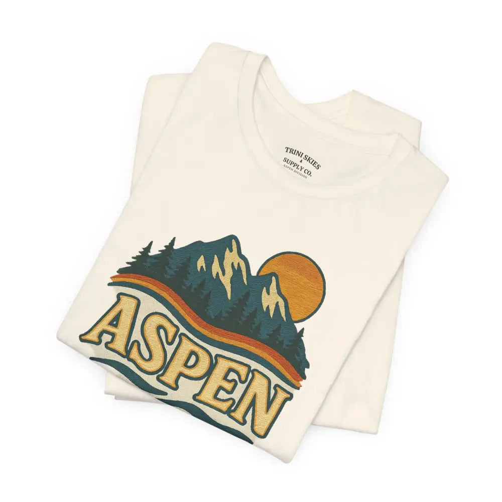 Cream-colored Aspen Lodge Tee with mountain, trees, sun, and drawn design features by Trini Skies Supply
