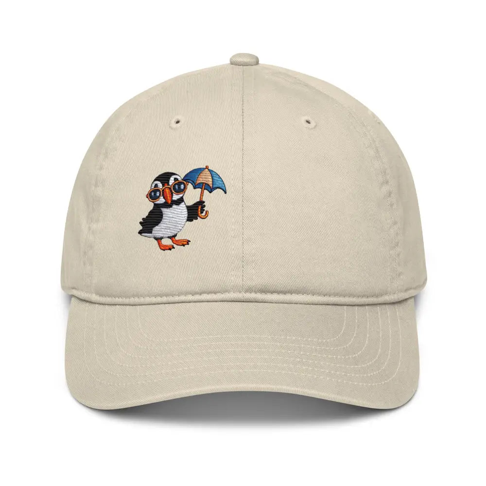 Light beige organic dad hat with embroidered playful puffin in sunglasses holding umbrella